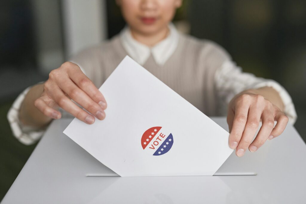 A person casting a vote by placing a ballot into a ballot box, symbolizing democratic participation.